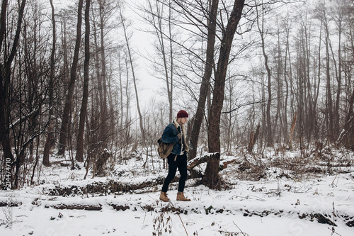 stylish hipster traveler with backpack in red hat walking in winter snowy forest. wanderlust and adventure concept with space for text. atmospheric moment. fashionable look.
