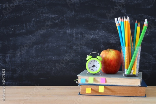 back to school concept. stack of books and pencils over wooden desk in front of blackboard.