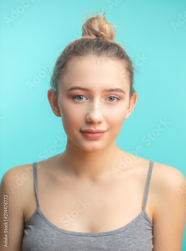 Attractive caucasian teenager girl with nude makeup, natural expressive  lips, perfect fresh skin posing isolated over blue studio background. Blond  hair tied in bun. Youth and Skin Care Concept. Stock Photo |