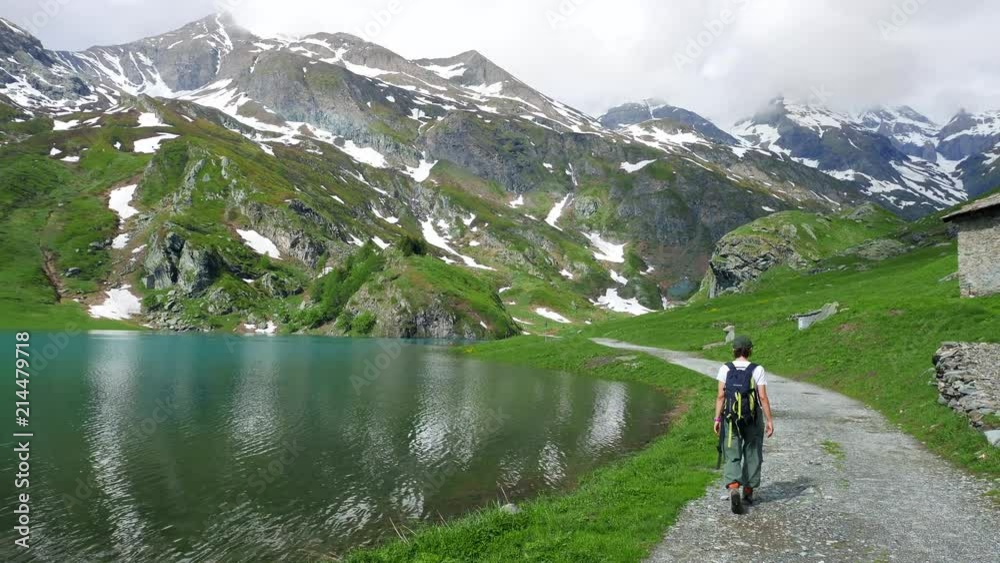 Woman hiking at blue lake on the Alps in summer, snowcapped mountain range, wanderlust concept Woman hiking at blue lake on the Alps in summer, snowcapped mountain range, wanderlust concept