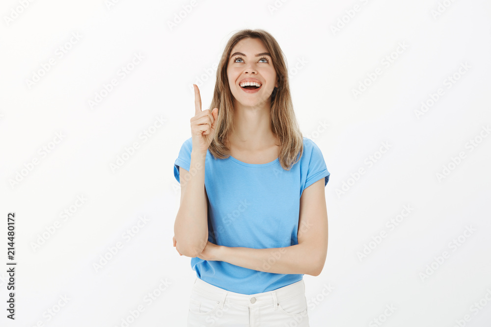 Girl standing on street seeing friend on balcony. Portrait of happy positive young and feminine woman with fair hair, pointing and looking up with bright smile, being interested with amusing thing Girl standing on street seeing friend on balcony. Portrait of happy positive young and feminine woman with fair hair, pointing and looking up with bright smile, being interested with amusing thing