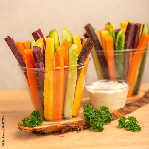 colorful carrots and cucumbers vegetables julienned in two plastic cups and sour cream dip decorated parsley over wooden board, concept of vegetarian healthy lifestyle