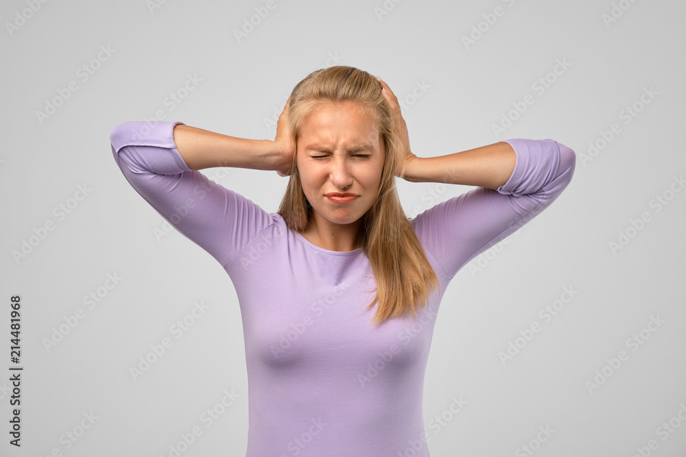 Portrait of attractive young woman in casual clothes covering her ears with hands not wanting to hear too loud sound. Pretty female wanting calm and silence trying to protect herself from noise Portrait of attractive young woman in casual clothes covering her ears with hands not wanting to hear too loud sound. Pretty female wanting calm and silence trying to protect herself from noise