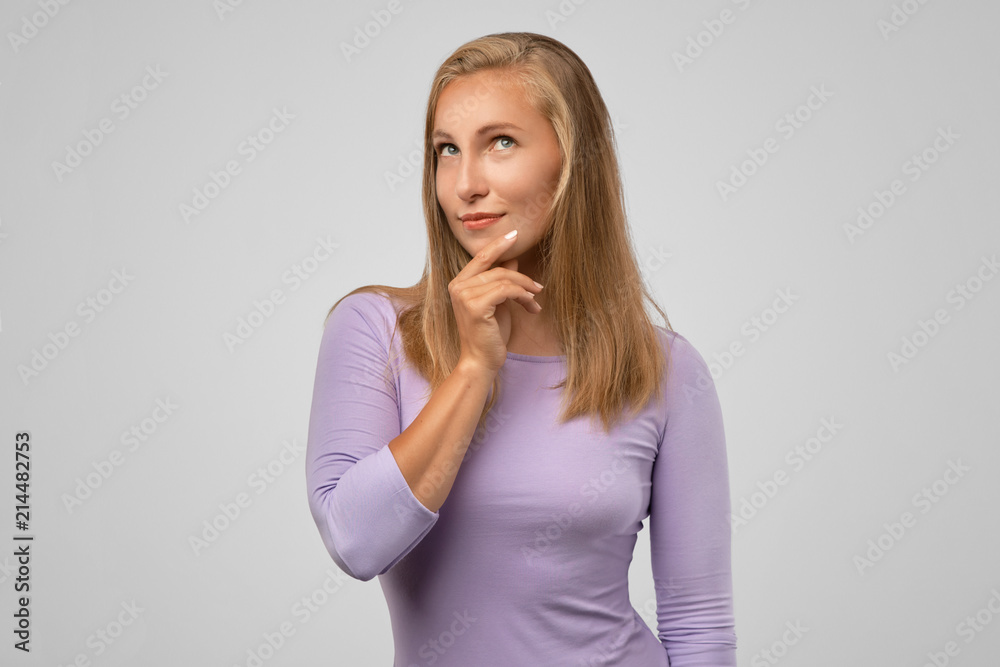 Portrait of pensive fair-haired dreamy blonde girl imagines something in her mind, looks upwards, being deep in thoughts, touching chin. Attractive young blonde female dreams about weekends Portrait of pensive fair-haired dreamy blonde girl imagines something in her mind, looks upwards, being deep in thoughts, touching chin. Attractive young blonde female dreams about weekends