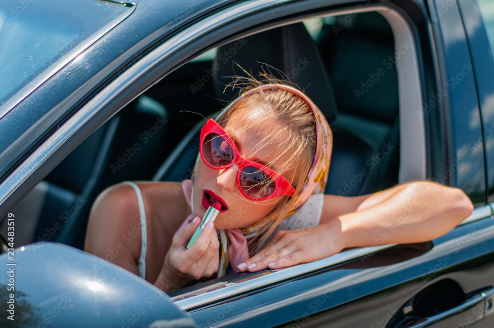 Beautiful fashion woman putting on lipstick while driving in the car.