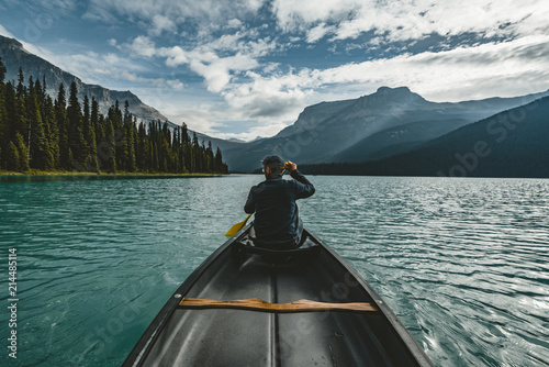 Young Man Canoeing on Emerald Lake in the rocky mountains canada with canoe and mountains in the background blue water.
