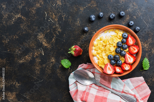 Corn flakes with milk, strawberries and blueberries on a dark background. View from above, flat lay. photo