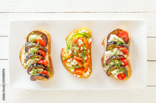 Bruschetta with fresh tomatoes and cheese, eggplant and mozzarella, sweet pepper and goat cheese on a white plate. Top view