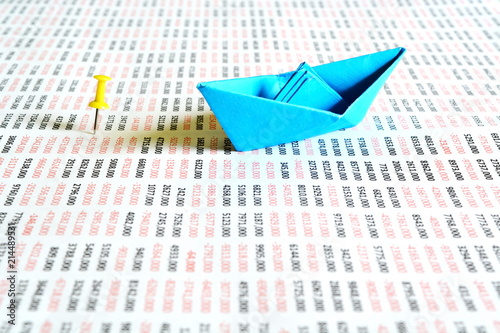 Origami paper blue boat on a big sheet of paper with large round numbers filled on it and yellow office pin