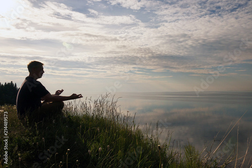 Man sitting in a Lotus position on top of a hill .