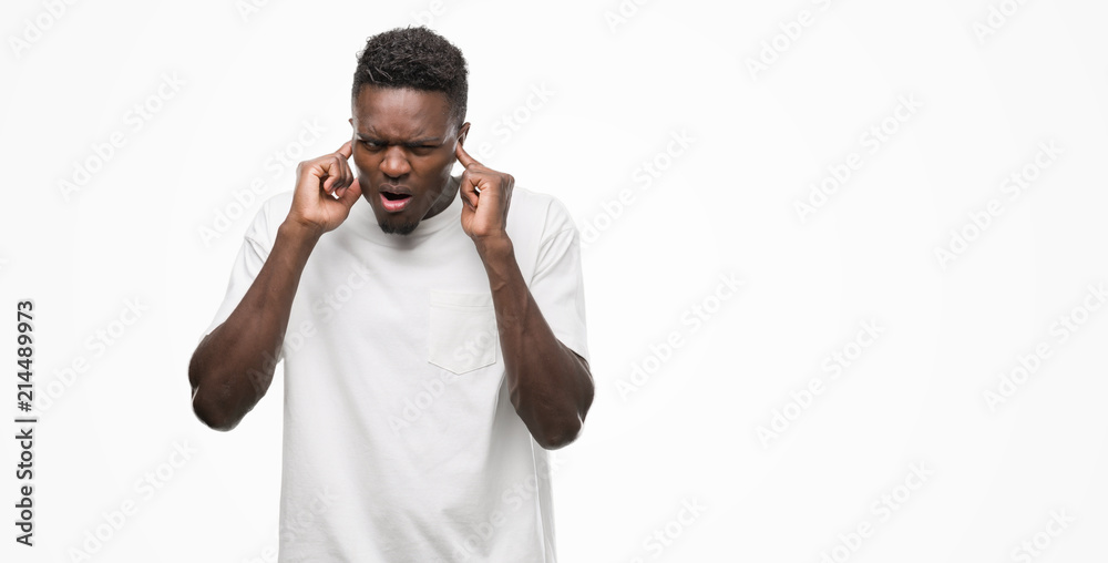 Young african american man wearing white t-shirt covering ears with fingers with annoyed expression for the noise of loud music. Deaf concept.