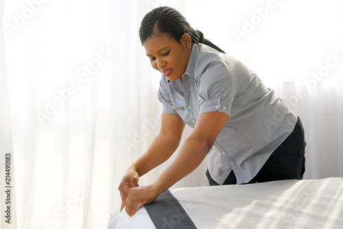 Maid making bed in hotel room. Staff Maid Making Bed. African housekeeper making bed.