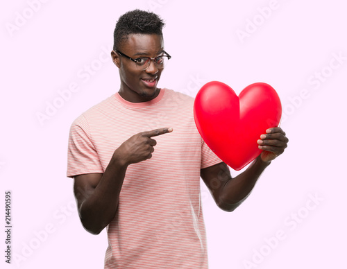Young african american man holding red heart very happy pointing with hand and finger © Krakenimages.com