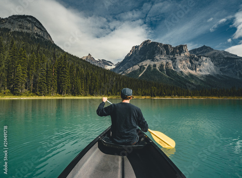 Canvas Print Young Man Canoeing on Emerald Lake in the rocky mountains canada with canoe and mountains in the background blue water