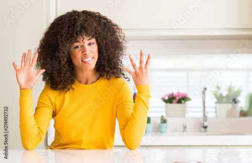 African american woman wearing yellow sweater at kitchen showing and pointing up with fingers number nine while smiling confident and happy.
