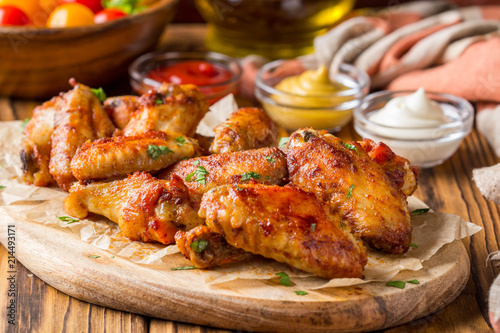 Fotografia Grilled chicken wings with ketchup and mustard sauces on wooden board
