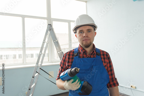 Happy white male builder with screwdriver infront of ladder, wearing white helmet.
