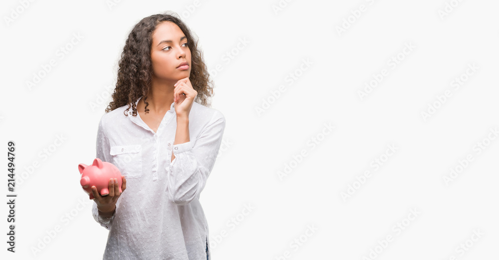 Young hispanic woman holding piggy bank serious face thinking about question, very confused idea Young hispanic woman holding piggy bank serious face thinking about question, very confused idea