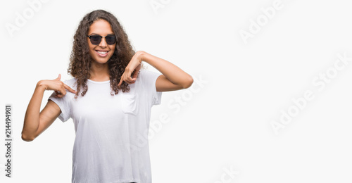 Young hispanic woman wearing sunglasses looking confident with smile on face, pointing oneself with fingers proud and happy.