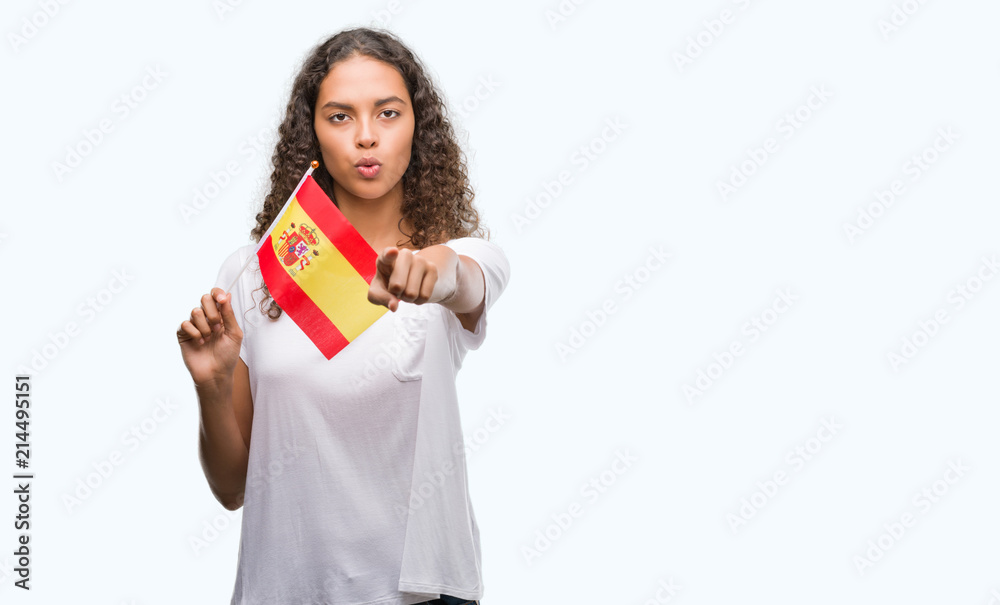 Young hispanic woman holding flag of Spain pointing with finger to the camera and to you, hand sign, positive and confident gesture from the front Young hispanic woman holding flag of Spain pointing with finger to the camera and to you, hand sign, positive and confident gesture from the front