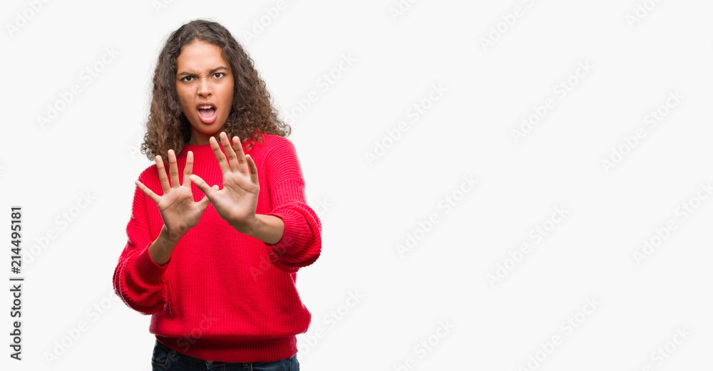 Fototapeta premium Young hispanic woman wearing red sweater afraid and terrified with fear expression stop gesture with hands, shouting in shock. Panic concept.