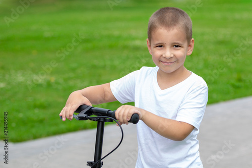 Portrait of a child outdoors. A happy boy is riding a scooter