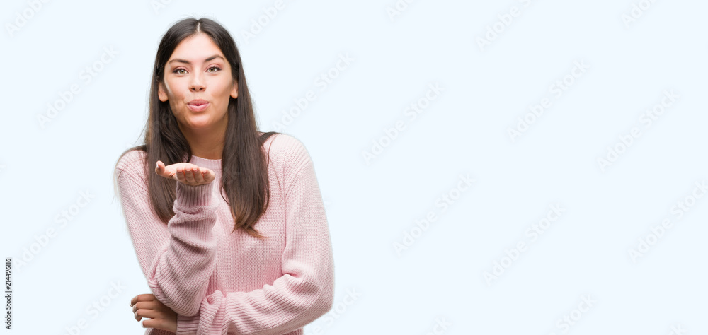 Young beautiful hispanic woman wearing a sweater looking at the camera blowing a kiss with hand on air being lovely and sexy. Love expression. Young beautiful hispanic woman wearing a sweater looking at the camera blowing a kiss with hand on air being lovely and sexy. Love expression.