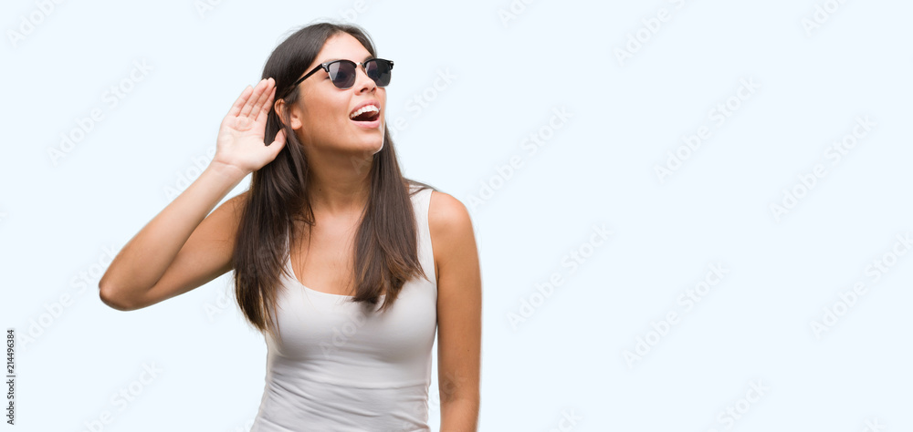 Young beautiful hispanic wearing sunglasses smiling with hand over ear listening an hearing to rumor or gossip. Deafness concept. Young beautiful hispanic wearing sunglasses smiling with hand over ear listening an hearing to rumor or gossip. Deafness concept.