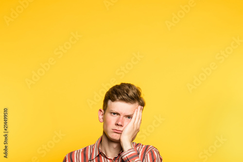 bored disinterested weariful indifferent unenthusiastic man. portrait of a young guy on yellow background popping up or peeking out from the bottom. copy space for advertisement. photo
