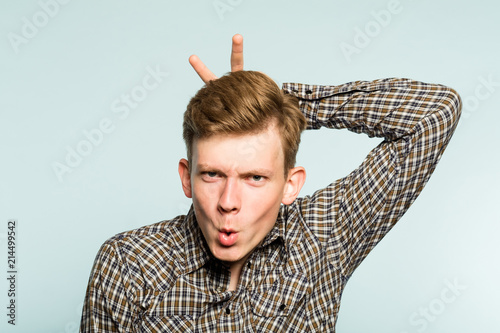 funny joyous happy frolic playful man fooling around giving bunny ears. portrait of a young guy on light background. emotion facial expression. feelings and people reaction. photo