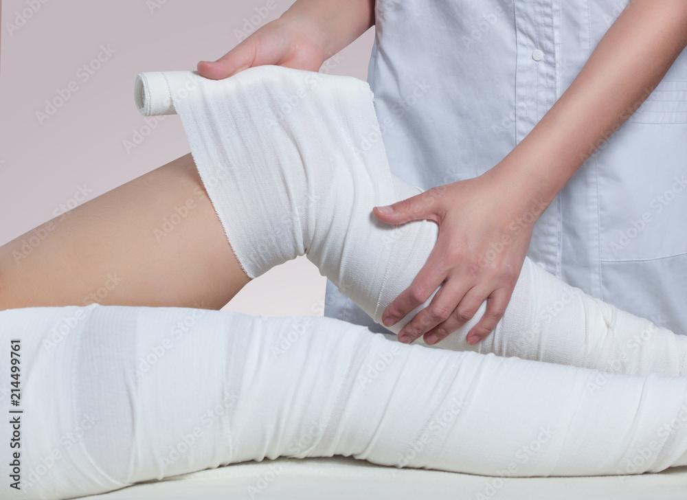 Fototapeta premium The cosmetologist wraps the leg of the customer. Anti-cellulite procedure-STYX wrap.