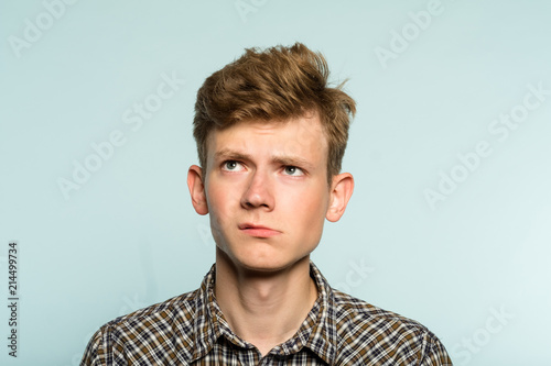 doubtful dubious uncertain hesitant man looking up thinking over smth. portrait of a young guy on light background. emotion facial expression. feelings and people reaction concept.