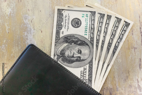 The United States one hundred-dollar bills in a black wallet laying on the shabby table surface photo