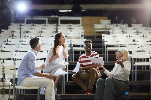 Foto Group of young colleagues with papers and their coach discussing screenplay in a