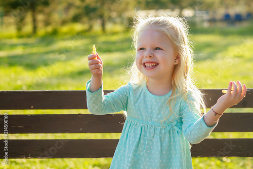 cute little blonde girl daughter eating french fries sitting on a bench in the park . unhealthy food in childhood