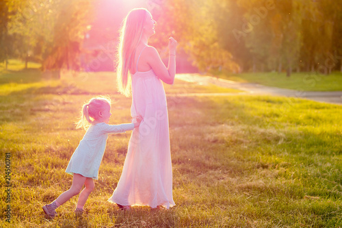 Game of tag .cute little blonde girl daughter in a blue dress with beautiful long-haired mother having fun and playing catch-up in summer day in field greens and grass background. happy children s Day