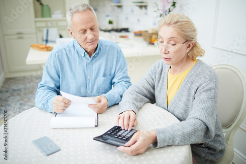 Mature wife with calculator and her husband making calculations of the last month expenses