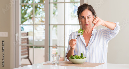 Middle aged woman eating fresh salad in a bowl at home with angry face  negative sign showing dislike with thumbs down  rejection concept