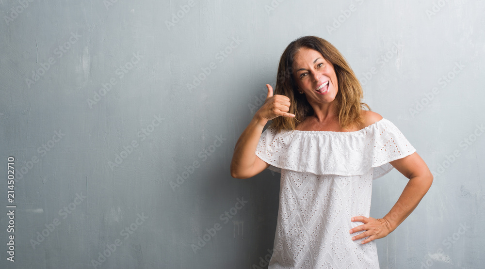 Middle age hispanic woman standing over grey grunge wall smiling doing phone gesture with hand and fingers like talking on the telephone. Communicating concepts. Middle age hispanic woman standing over grey grunge wall smiling doing phone gesture with hand and fingers like talking on the telephone. Communicating concepts.