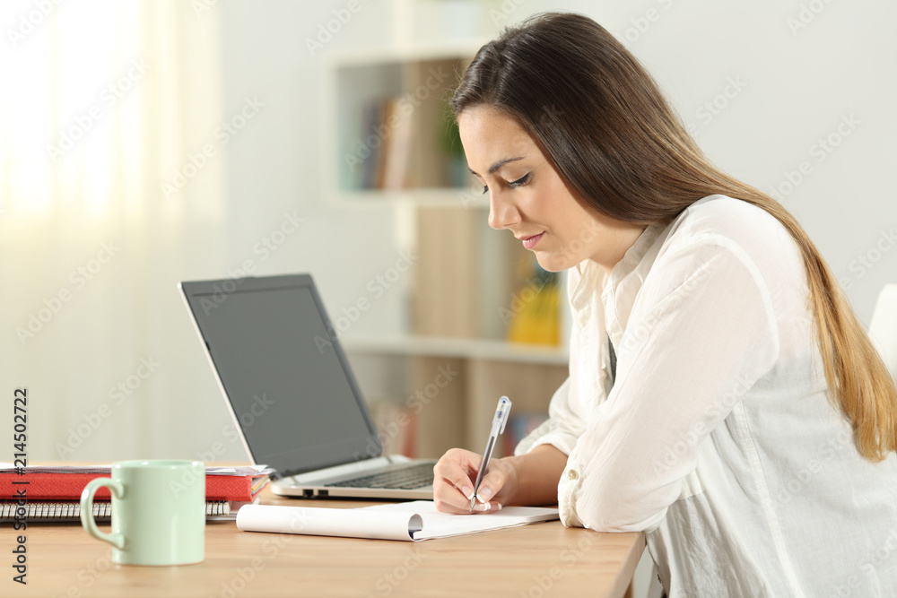 Student taking notes in a notebook on a table Student taking notes in a notebook on a table