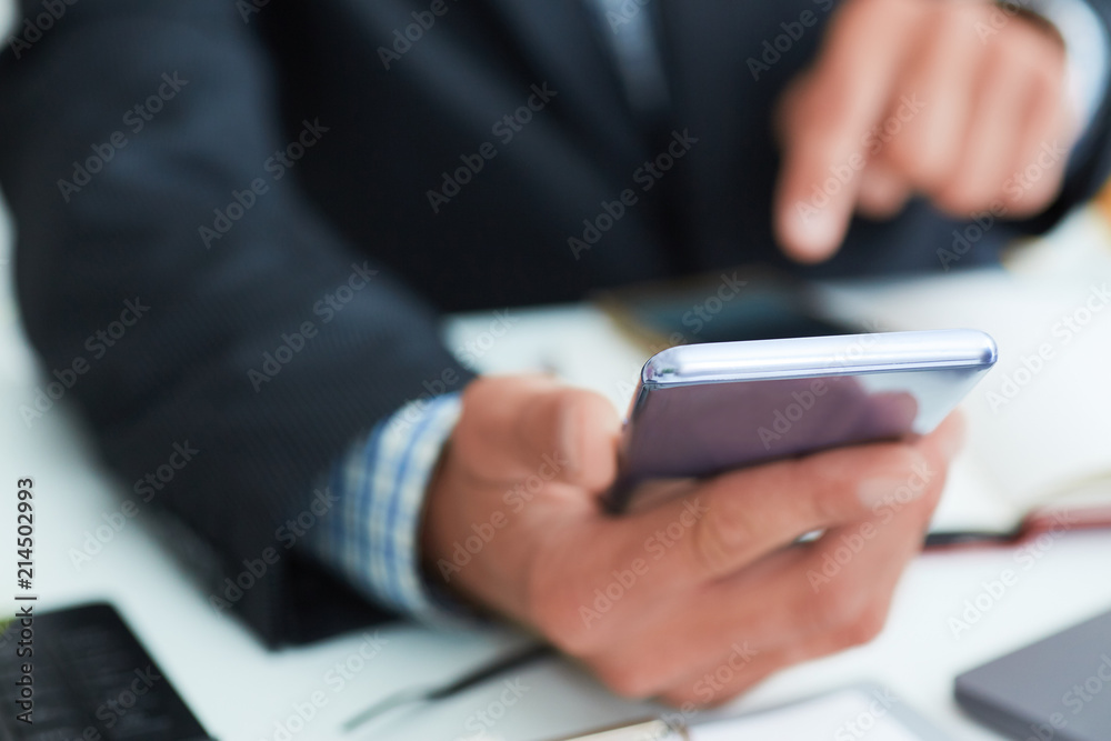Top view shot of a man's hands in suit using smart phone in office interior, business man hands using cell phone at office desk. Top view shot of a man's hands in suit using smart phone in office interior, business man hands using cell phone at office desk.
