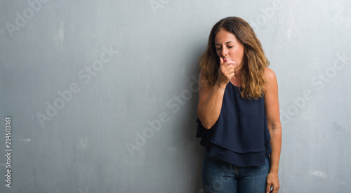 Middle age hispanic woman standing over grey grunge wall feeling unwell and coughing as symptom for cold or bronchitis. Healthcare concept.