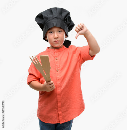 Dark haired little child wearing chef uniform with angry face, negative sign showing dislike with thumbs down, rejection concept