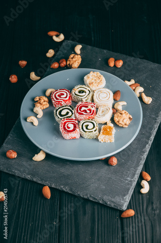 Traditional oriental sweets and nuts: hazelnuts, cashews on a dark wooden background. Turkish dessert is the Rakhat locus. View from above. Place under the text.