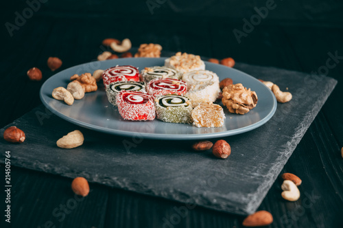Traditional oriental sweets and nuts: hazelnuts, cashews on a dark wooden background. Turkish dessert is the Rakhat locus. View from above. Place under the text.