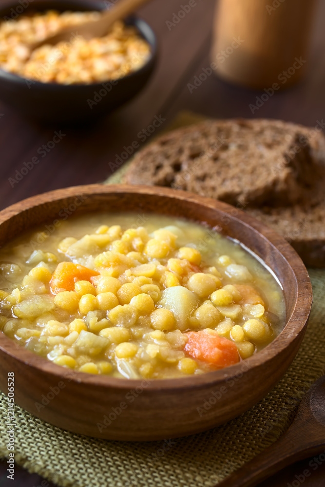 Vegetarian and vegan yellow split pea soup or stew with potato, carrot and celery in wooden bowl, photographed with natural light (Selective Focus, Focus in the middle of the soup) Vegetarian and vegan yellow split pea soup or stew with potato, carrot and celery in wooden bowl, photographed with natural light (Selective Focus, Focus in the middle of the soup)