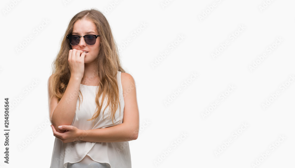 Young blonde woman wearing sunglasses looking stressed and nervous with hands on mouth biting nails. Anxiety problem. Young blonde woman wearing sunglasses looking stressed and nervous with hands on mouth biting nails. Anxiety problem.