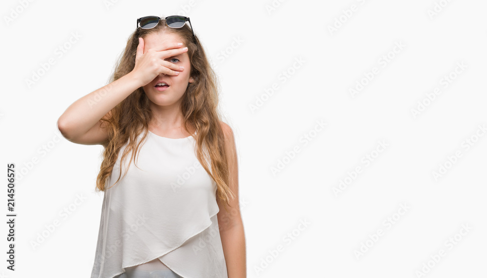 Young blonde woman wearing sunglasses peeking in shock covering face and eyes with hand, looking through fingers with embarrassed expression. Young blonde woman wearing sunglasses peeking in shock covering face and eyes with hand, looking through fingers with embarrassed expression.