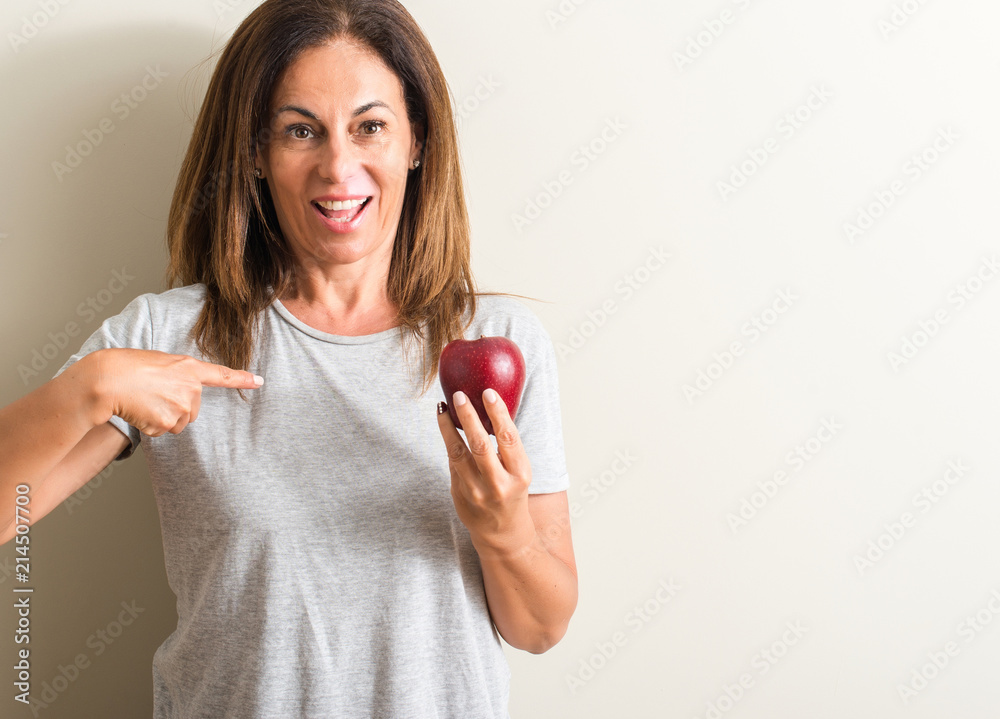 Middle age woman holding a green apple with surprise face pointing finger to himself Middle age woman holding a green apple with surprise face pointing finger to himself