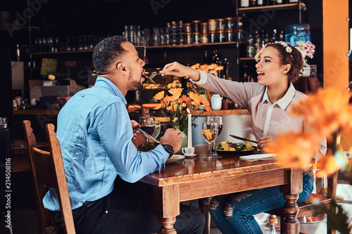 Beautiful African-American couple in love having a great time together at their dating  an attractive couple enjoying each other  young woman feeding her man in restaurant.